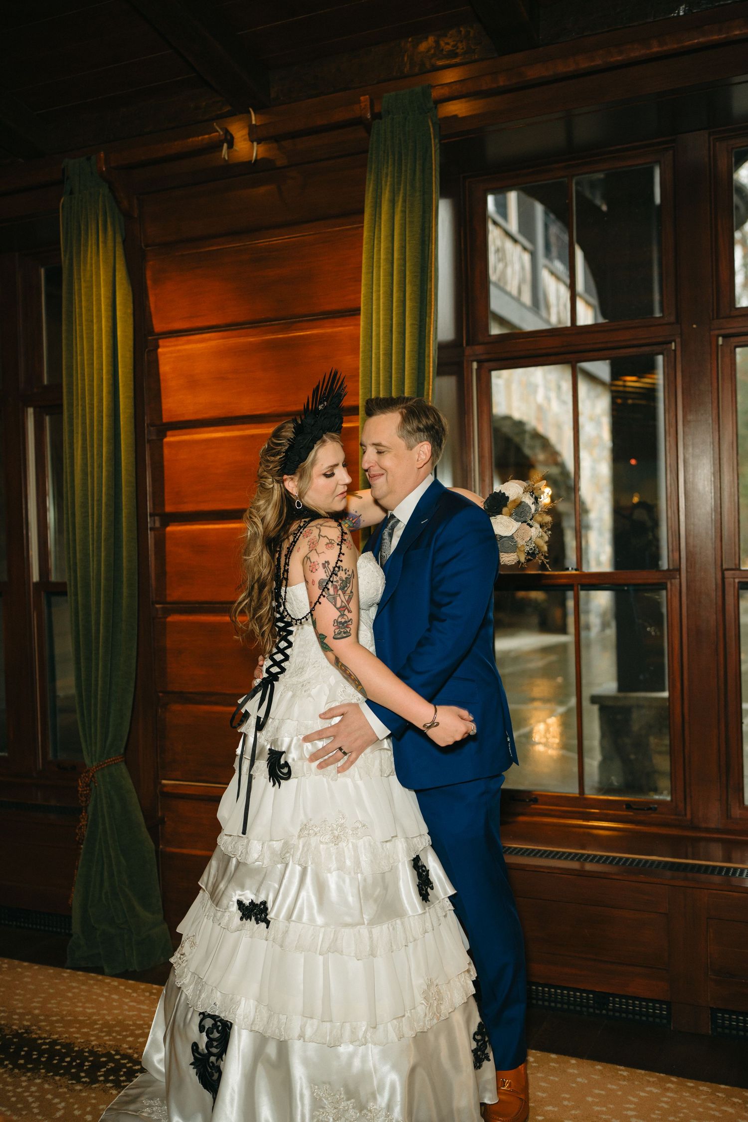 A couple shares their first dance in a rustic venue with wood paneling and green curtains.