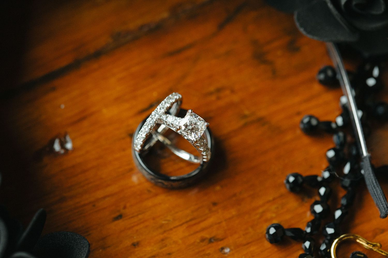 A sparkling engagement ring with diamonds sits on a wooden surface next to black decorative elements.