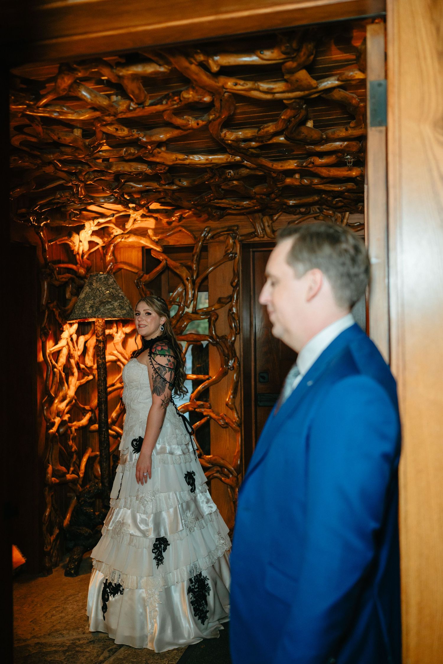 A couple stands in a rustic venue with dramatic lighting and branches decorating the ceiling.