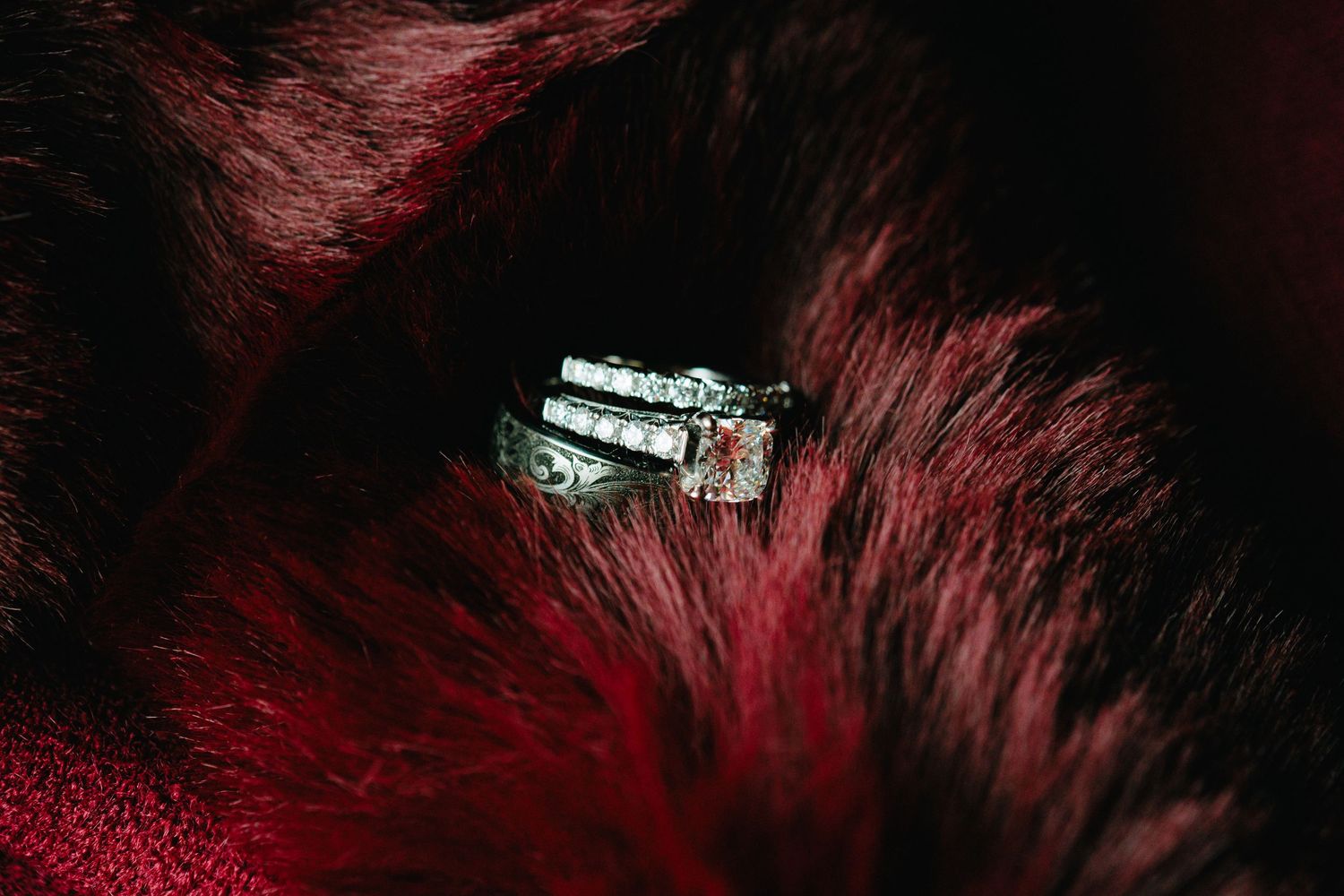 Diamond engagement ring nestled in rich red fur fabric with dramatic lighting.