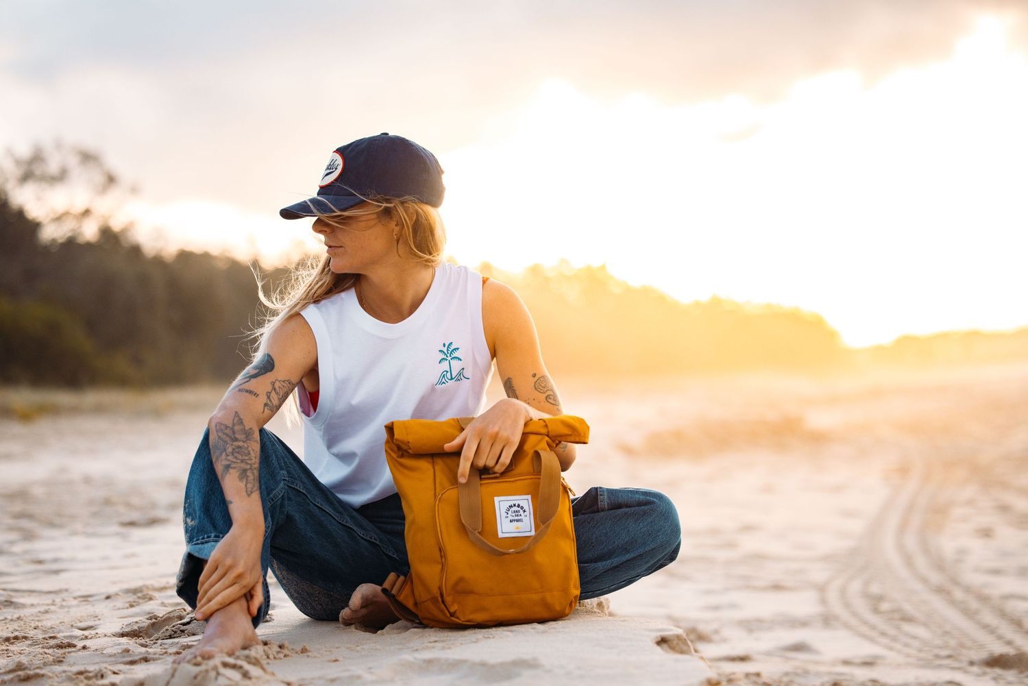 Person sitting on beach with orange backpack during sunset.