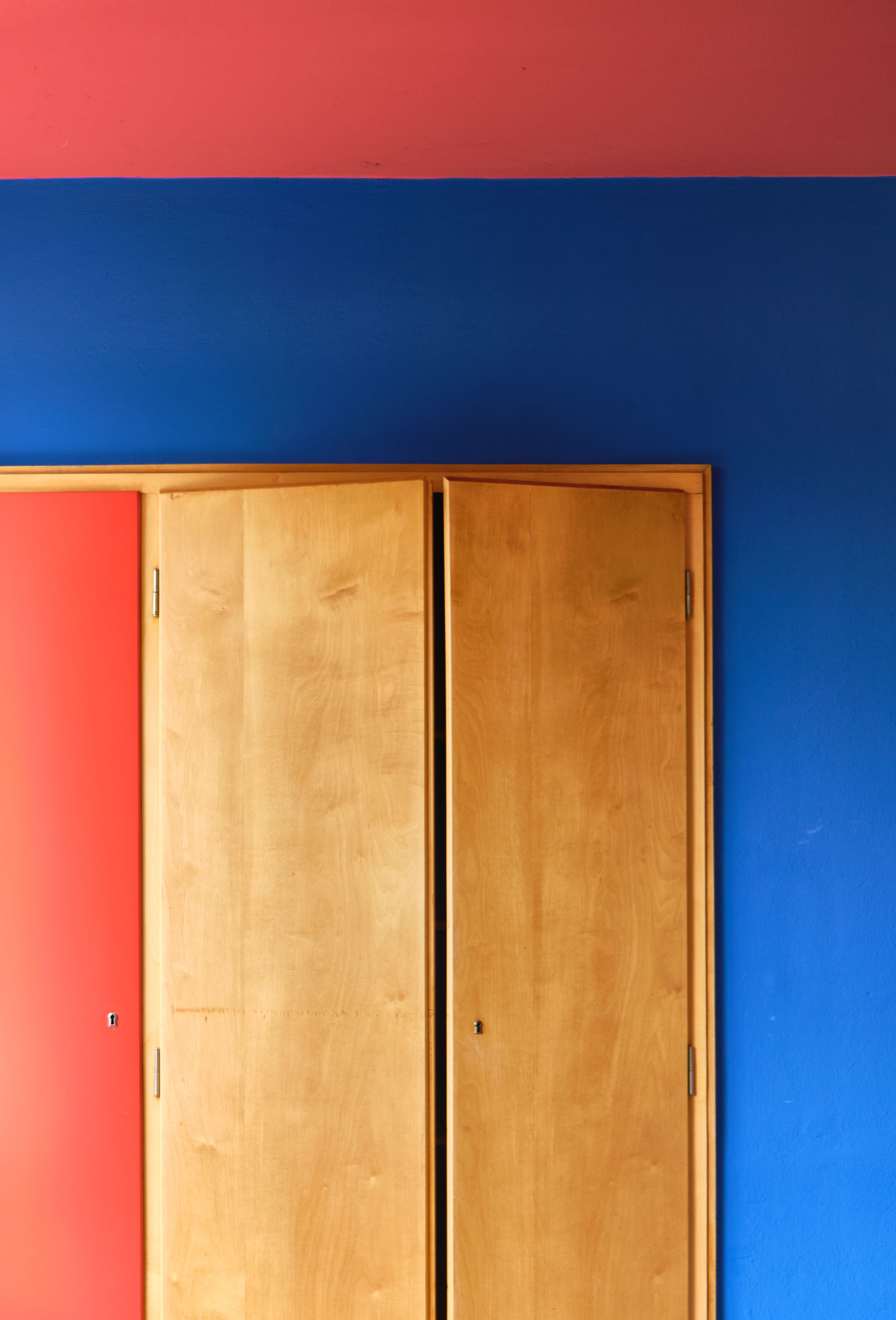 Minimalist architectural detail showing a wooden door against red and blue walls in a geometric composition.