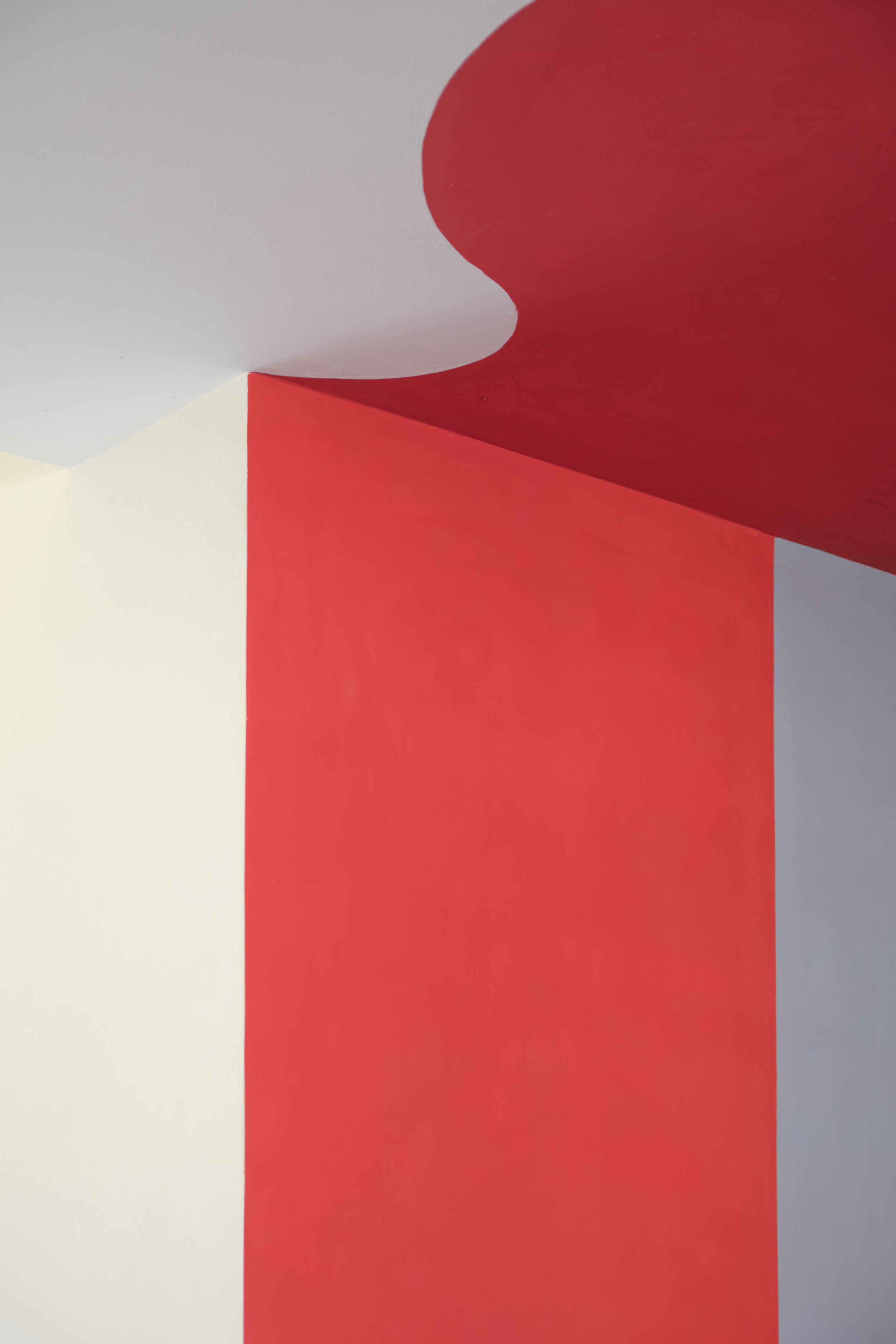 Abstract architectural detail showing a curved red wall against a white surface creating bold geometric shapes and shadows.