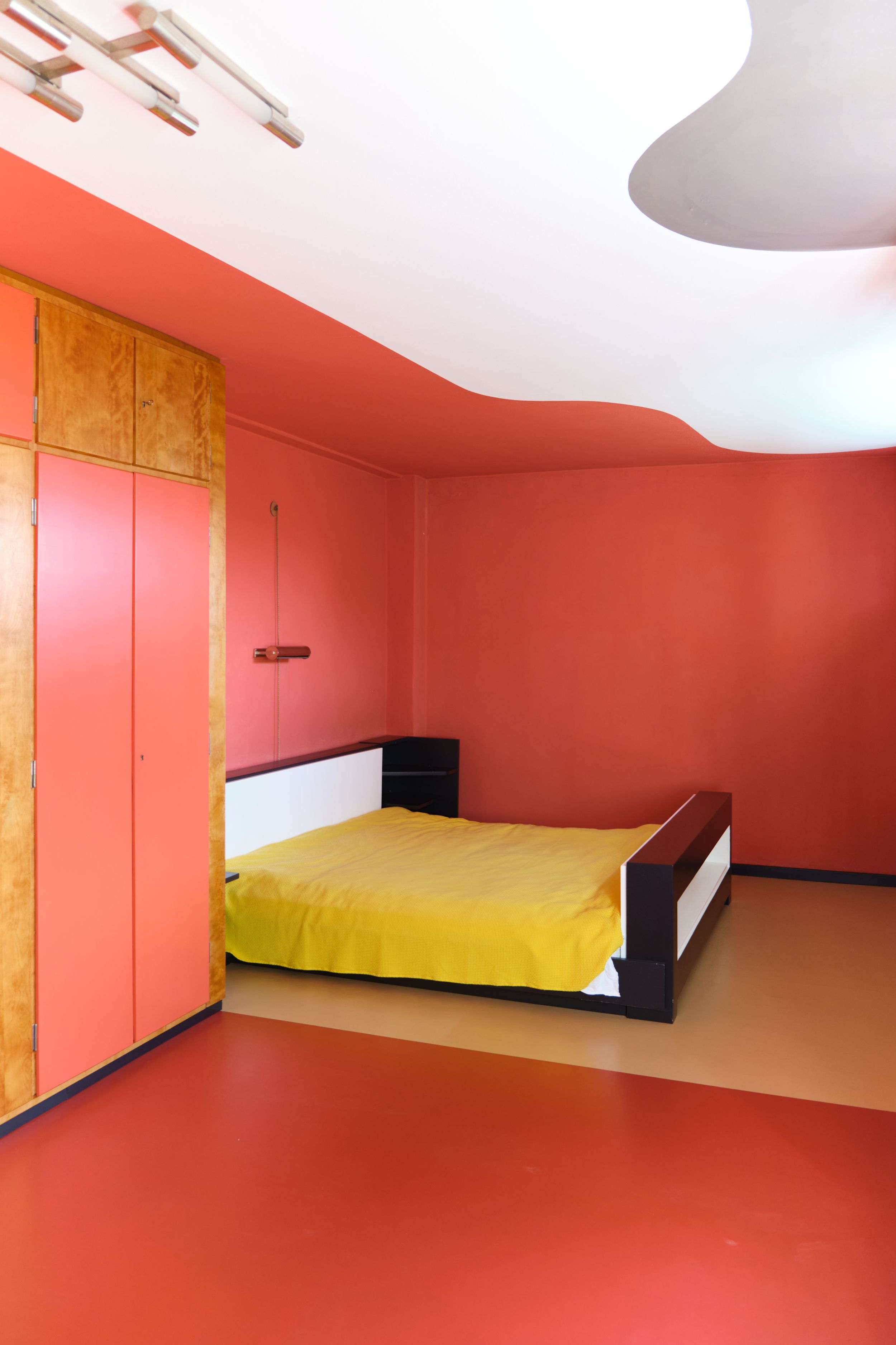 Modern bedroom interior with pink walls, yellow bedding, and minimalist design features across three connected views.