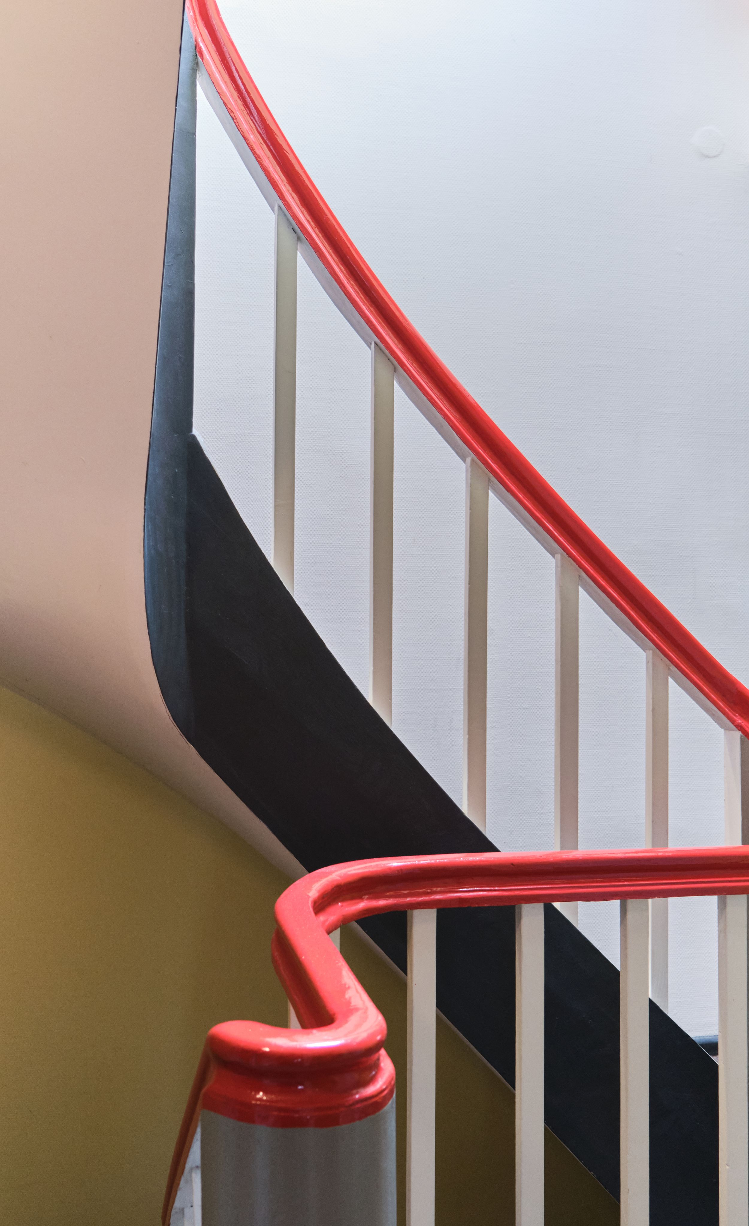Modern staircase with red handrail, white spindles, and black accent wall creating a bold geometric design.