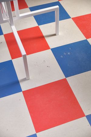 A geometric floor pattern with red, white and blue squares and white metal table legs casting shadows.