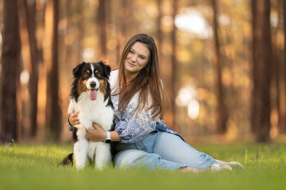 Person relaxing outdoors on grass with an Australian Shepherd dog during golden hour sunset.