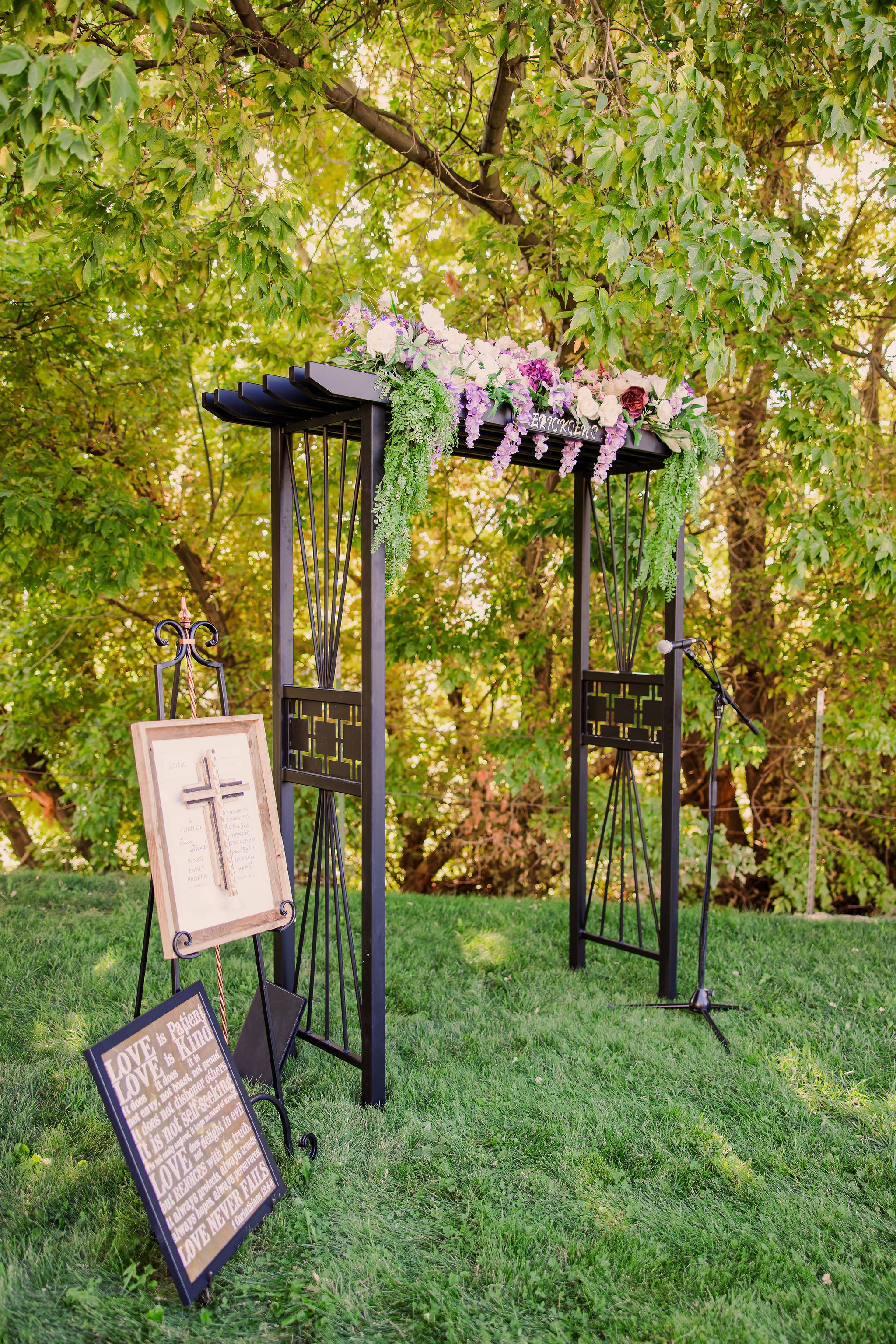 A series of black metal lanterns with pink decorative signs displayed in a garden setting with green trees in the background.