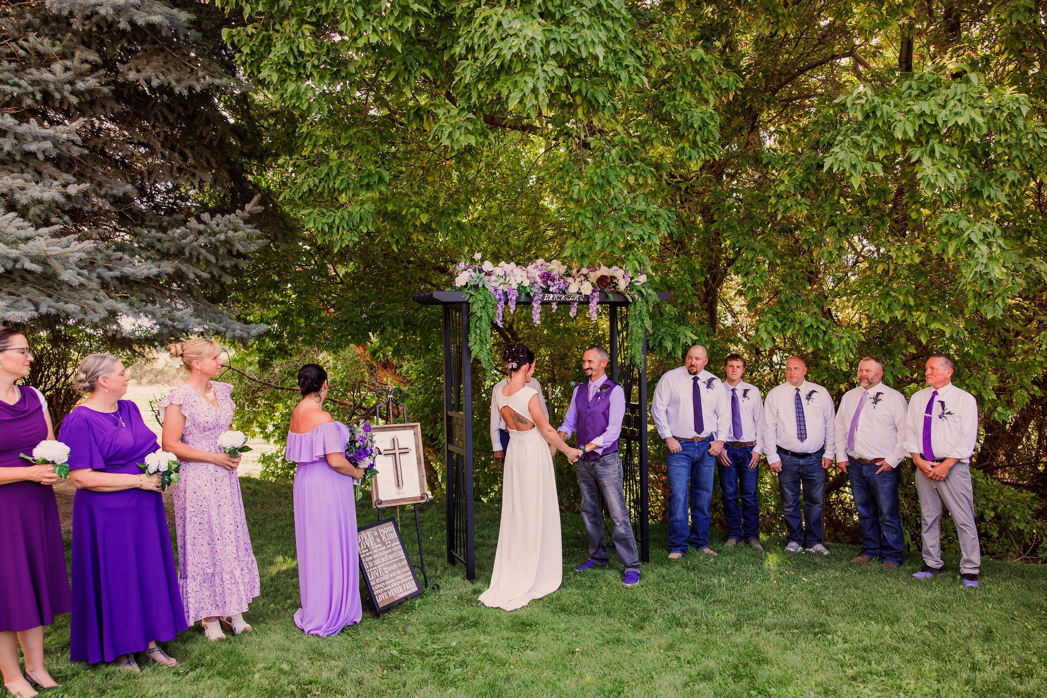 Wedding party in purple and pink attire poses together in a garden setting during golden hour.