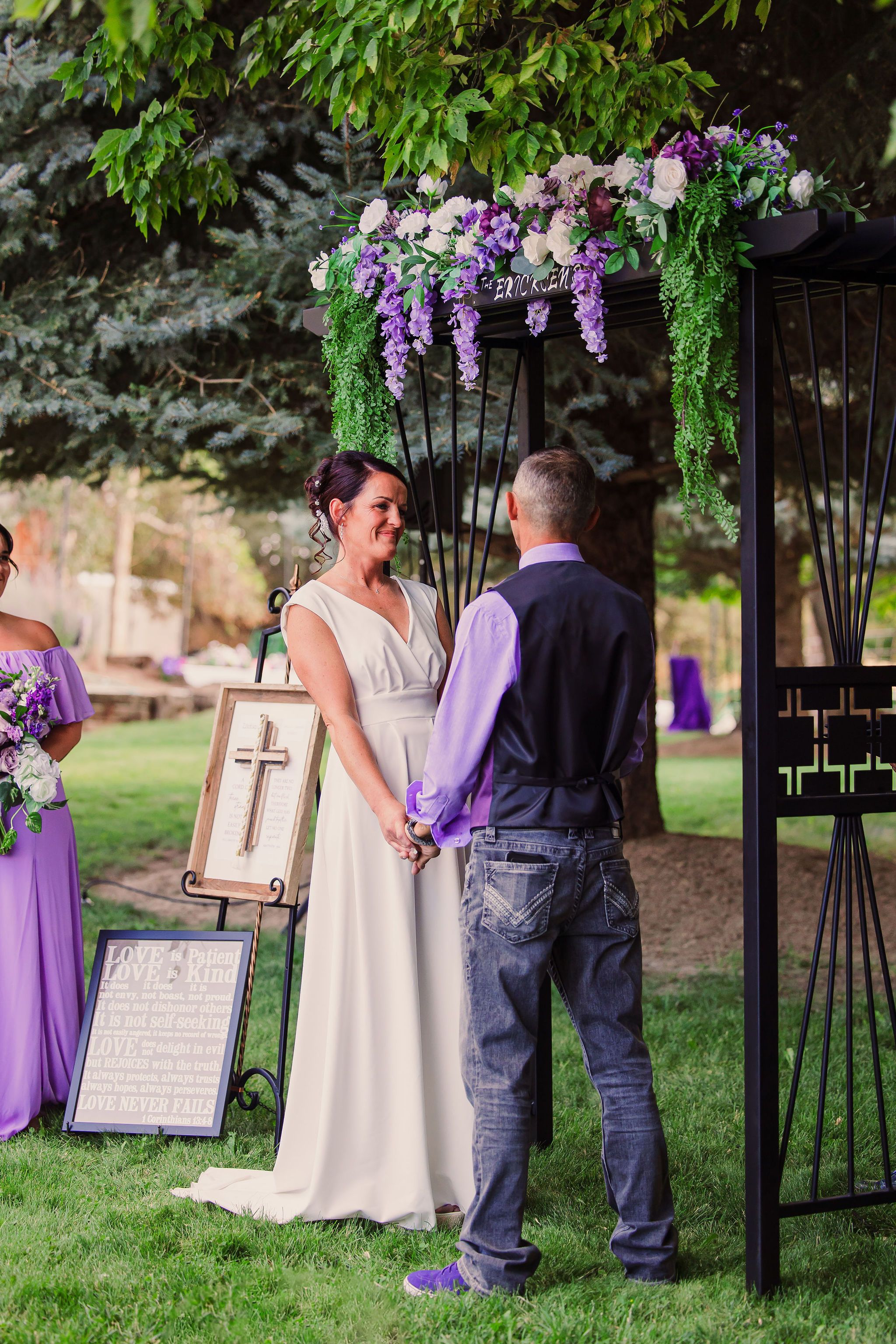A wedding memorial display with purple floral arrangements and signage stands in a garden setting.