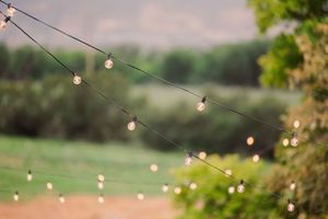 String lights hang across an outdoor wedding venue with green rolling hills and trees in the background.