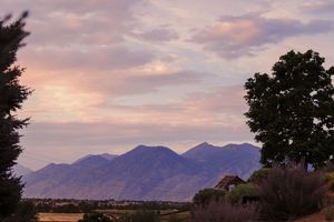 A panoramic view of mountains silhouetted against a purple and orange sunset sky with trees in the foreground.