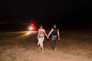 A group of people walk along a dark beach at night with flashlights illuminating their path.