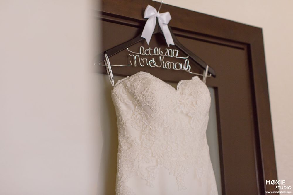A white wedding dress hangs on a personalized hanger against a brown door.
