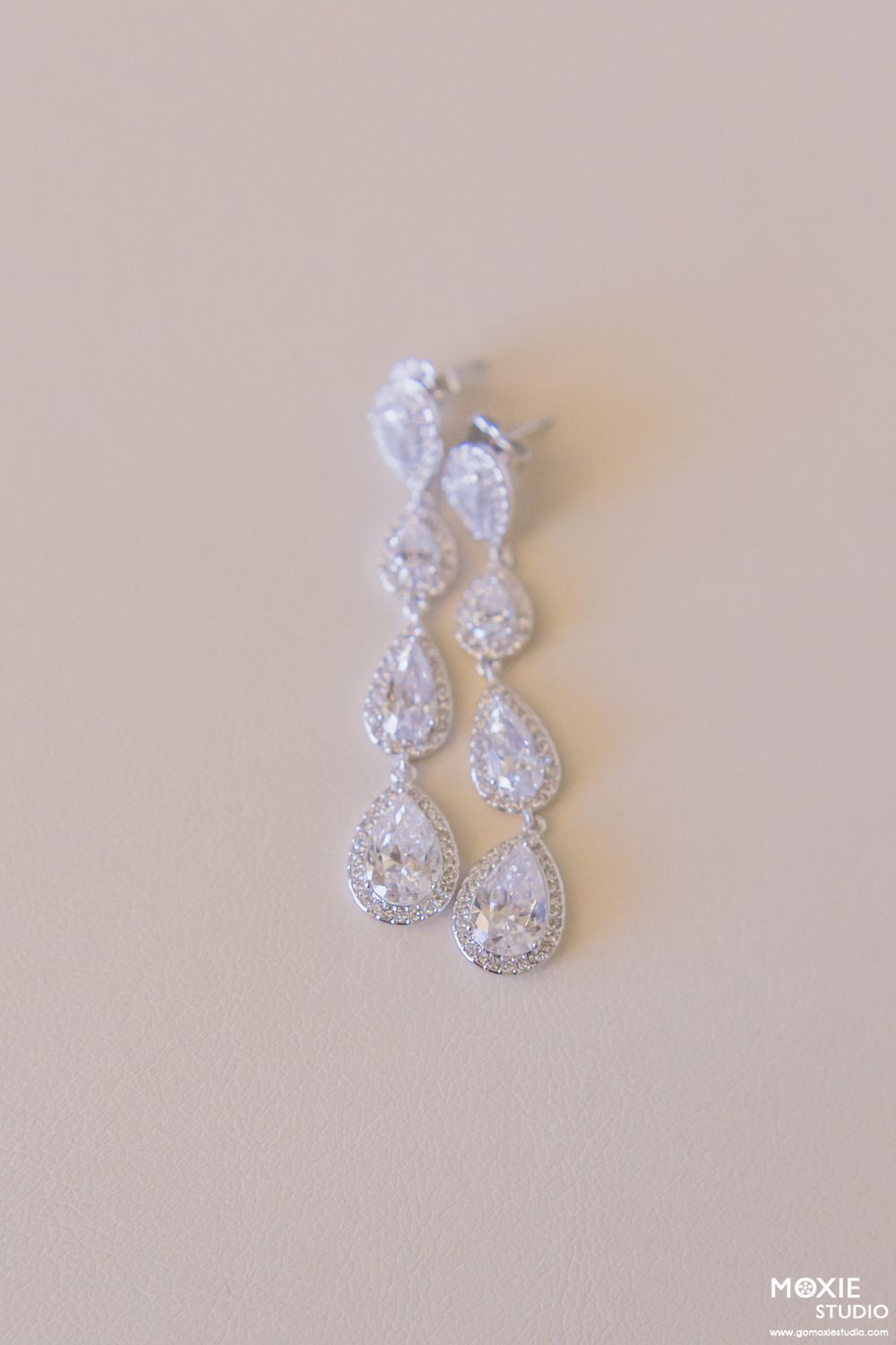 Elegant teardrop crystal wedding earrings on a light beige background.