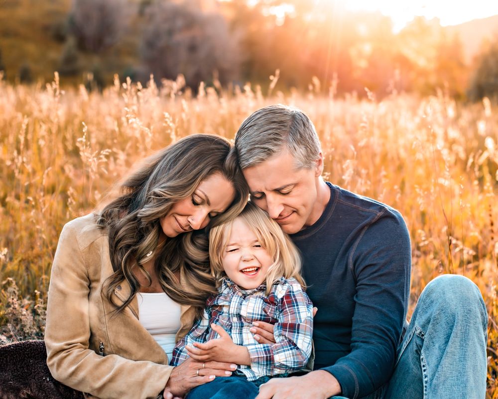 Mom and Dad cuddling their toddler sun in a field at Lair o the Bear Park
