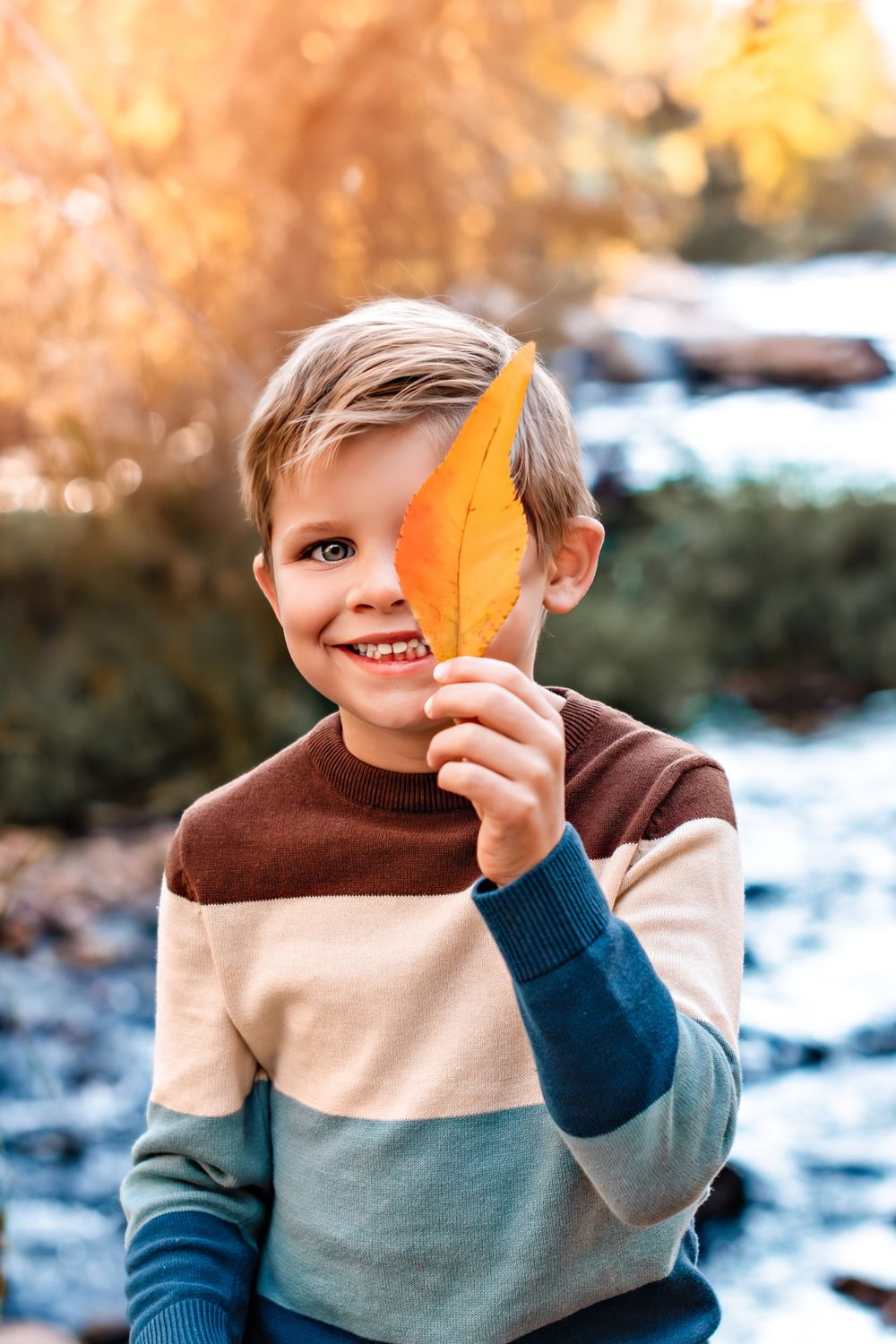 6 year old boy holding a fall leaf in front of his eye for a photo