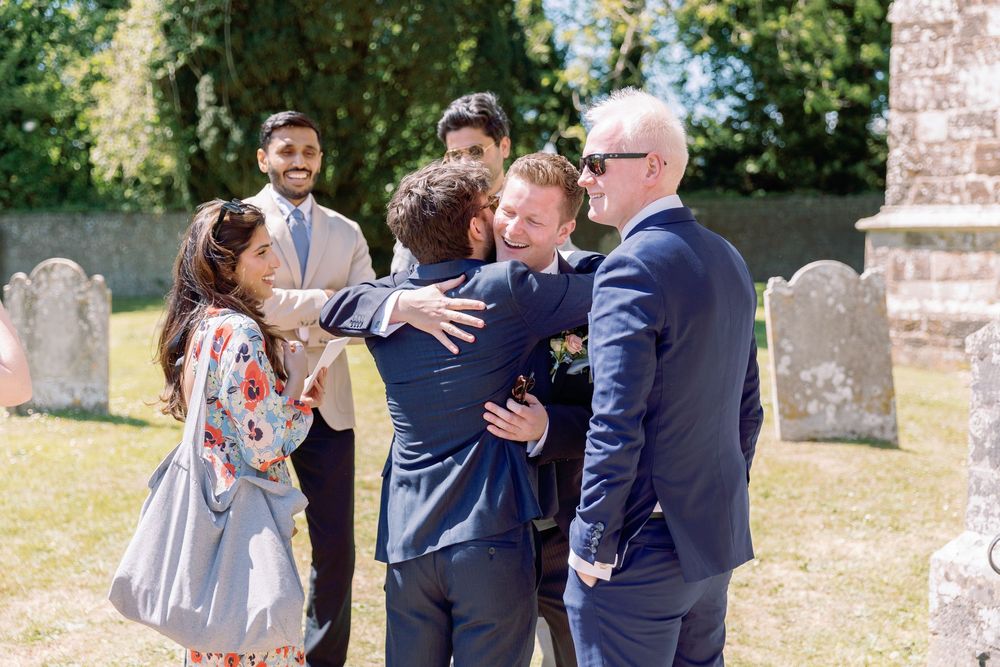 Wedding guests sharing joyful moments and embraces outside a church on a sunny day.