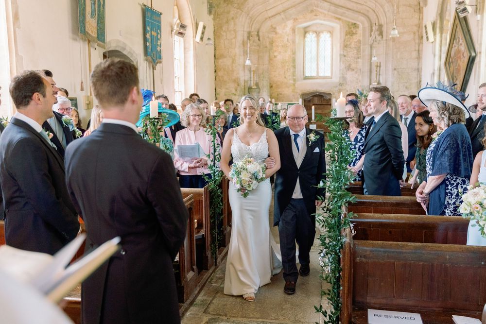 Wedding ceremony in progress inside historic stone church with greenery-decorated aisle.