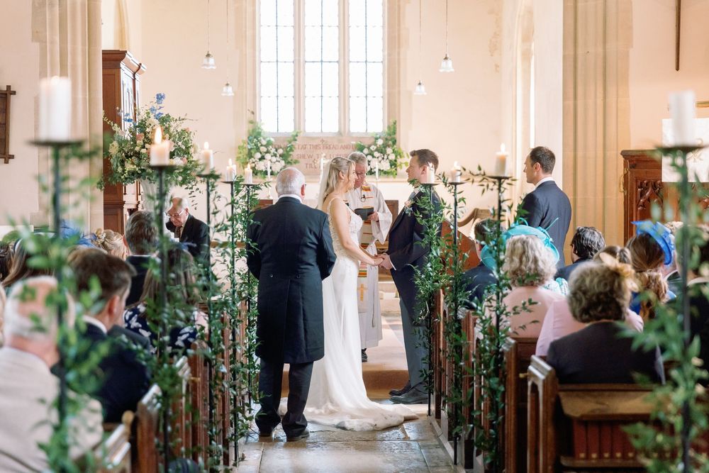 Wedding ceremony in a bright church with floral arch decorations and string lights.