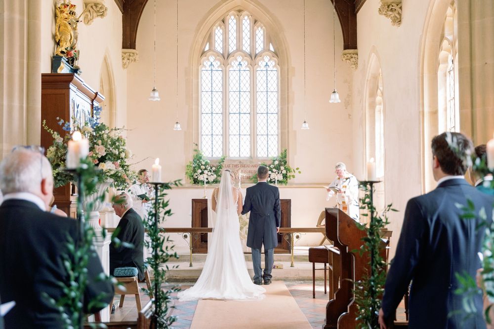 Intimate wedding ceremony in bright church sanctuary with floral arrangements and gothic windows.