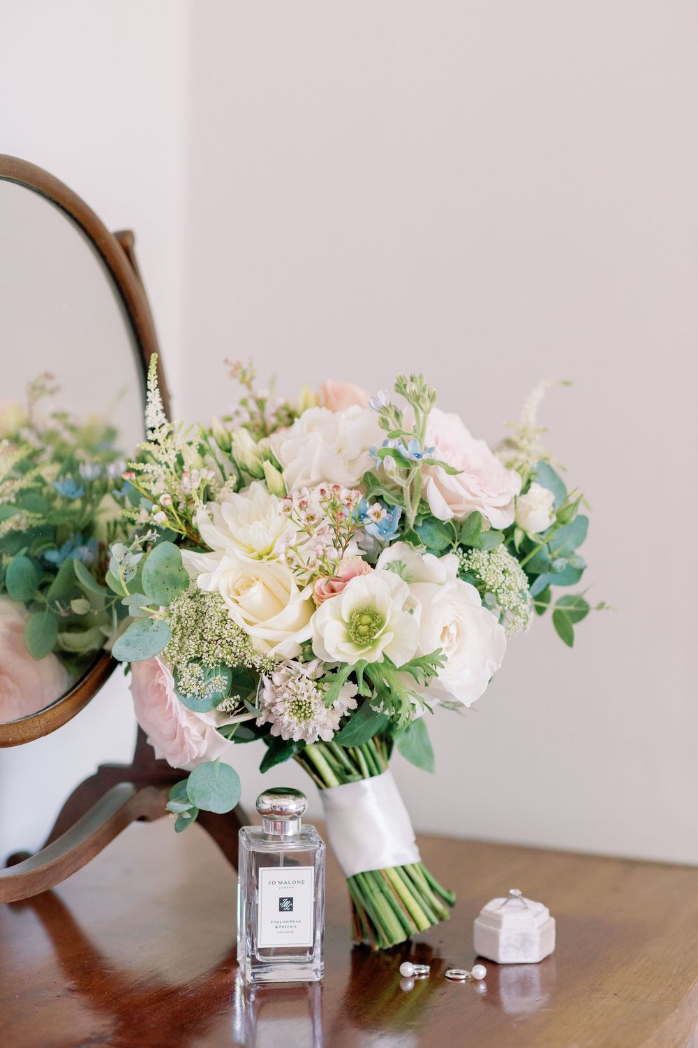 Elegant bridal bouquet with white roses and eucalyptus next to perfume bottle and mirror.