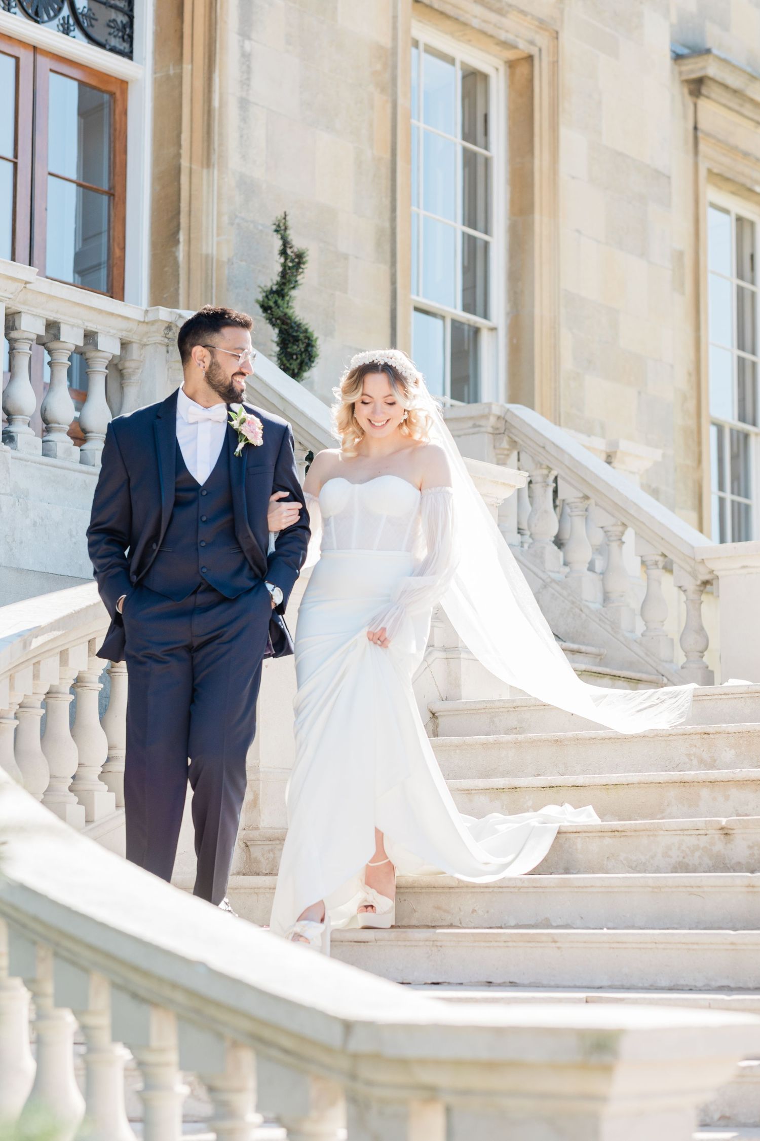 Elegant bride and groom pose on grand marble staircase at historic estate during romantic wedding photoshoot.