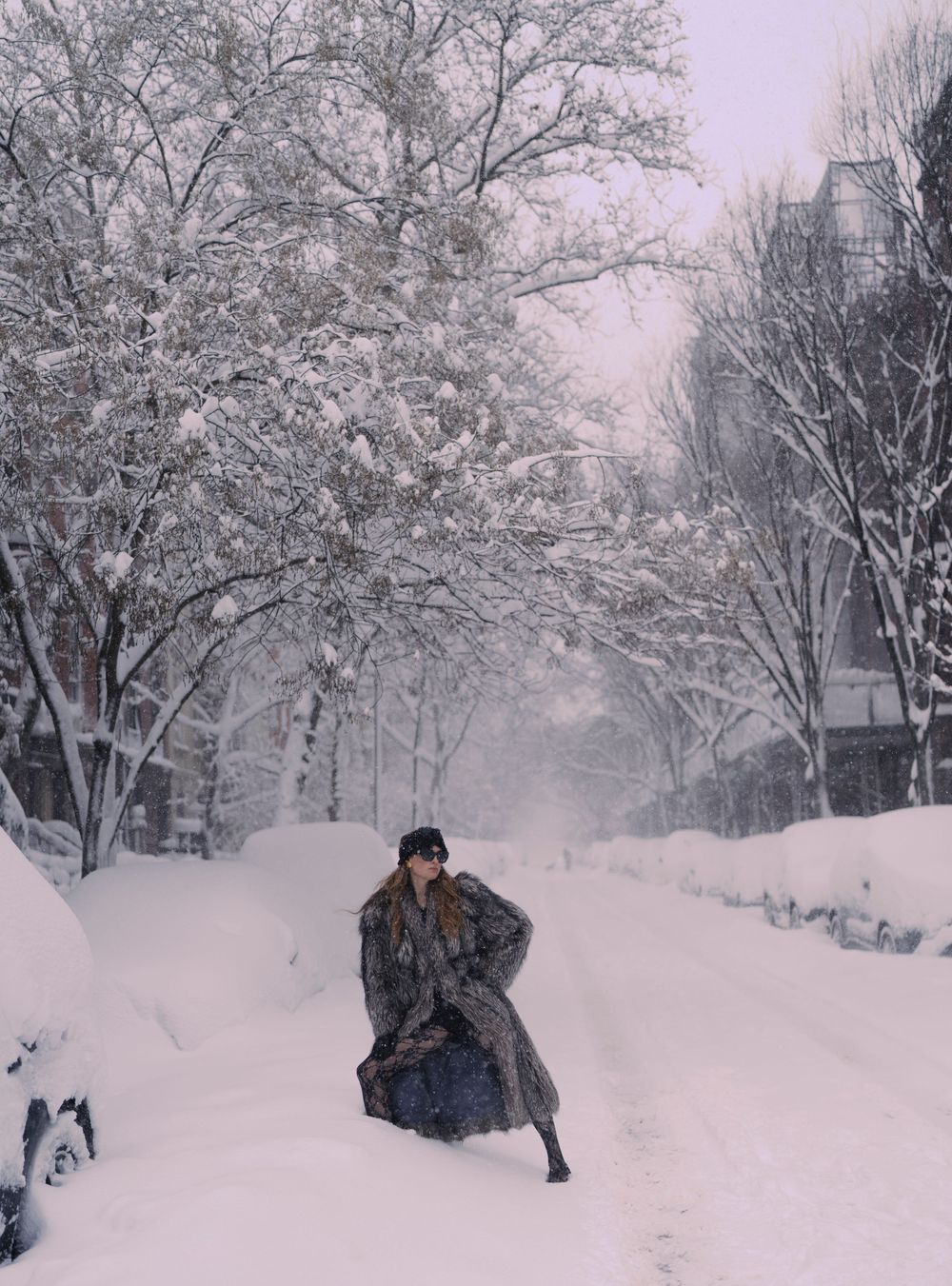A figure in a long coat walks through a snow-covered street lined with frost-covered trees in winter.