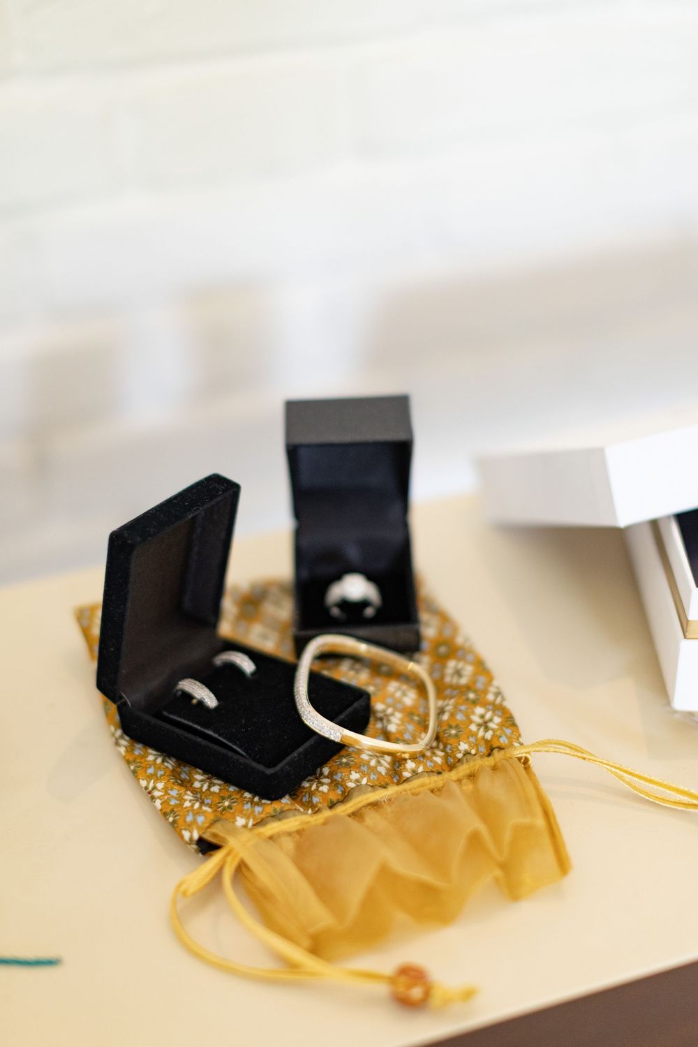 Wedding rings displayed in black boxes on a gold sequined drawstring pouch.