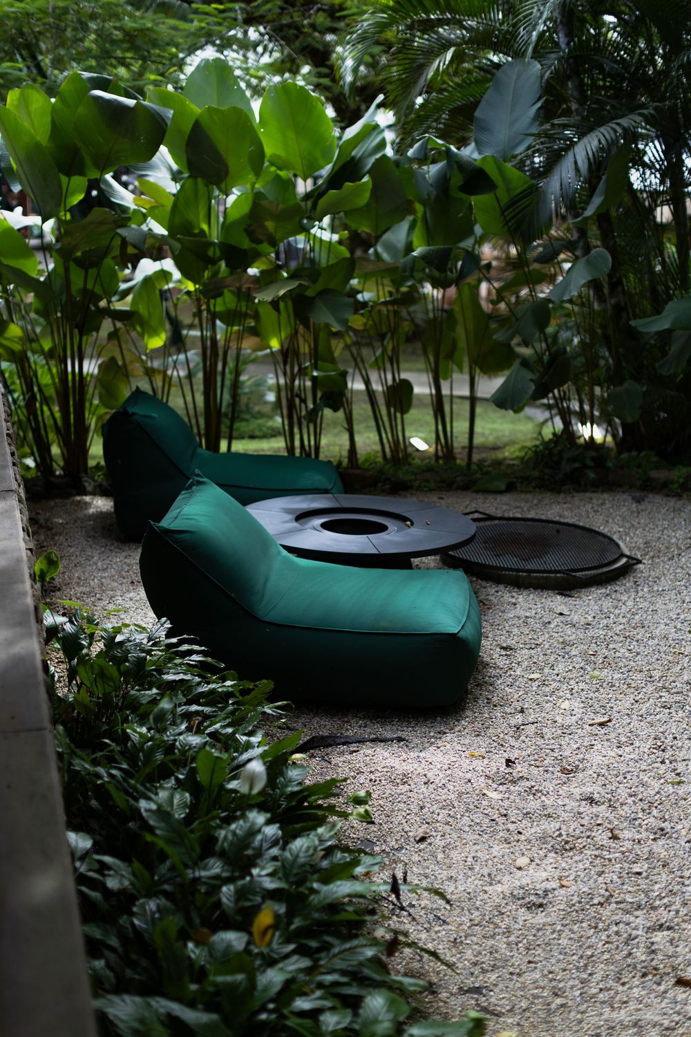 Curved green outdoor bean bag chairs arranged on a gravel path surrounded by tropical plants and palm trees.