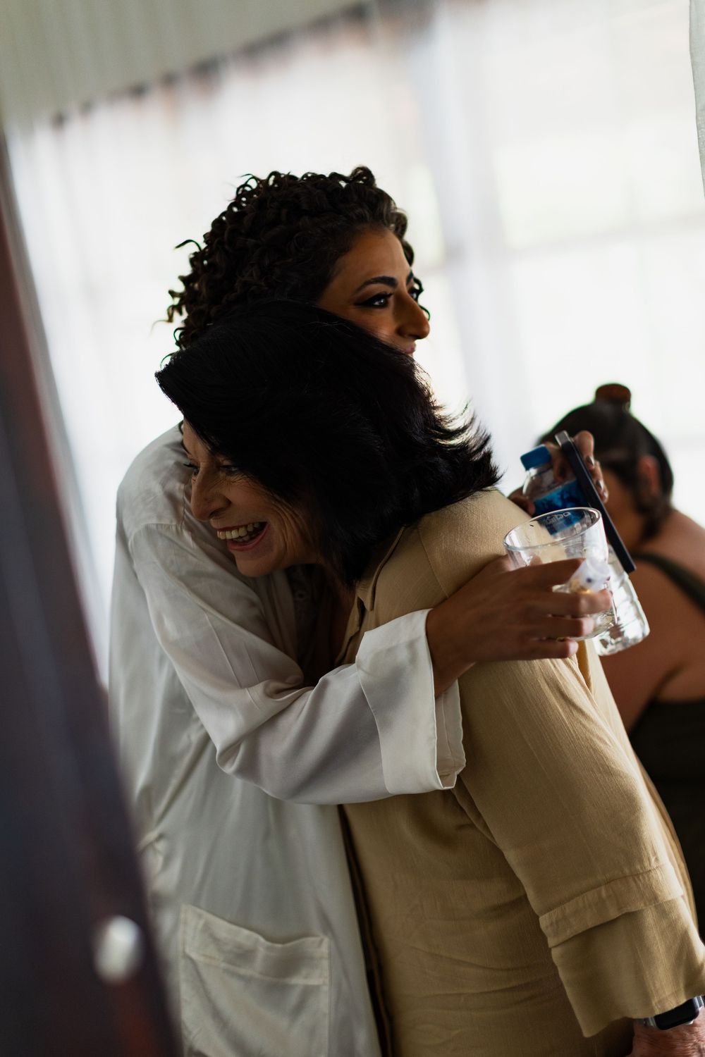 People sharing warm embraces and hugs in a bright indoor setting with natural lighting.