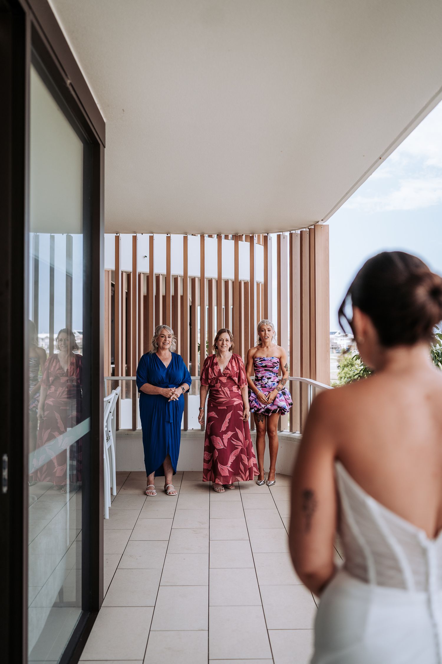 A group gathers on a modern balcony with glass walls and wooden slat details during what appears to be a special occasion.