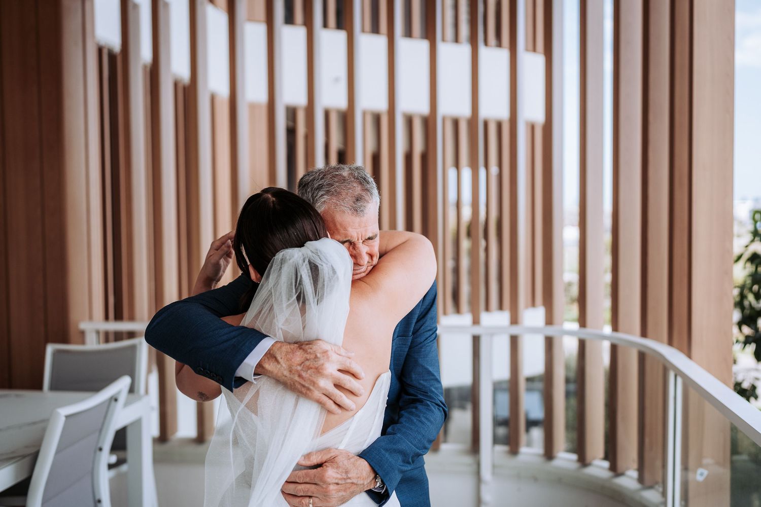 A couple shares a tender embrace in a modern interior space with wooden slat walls.