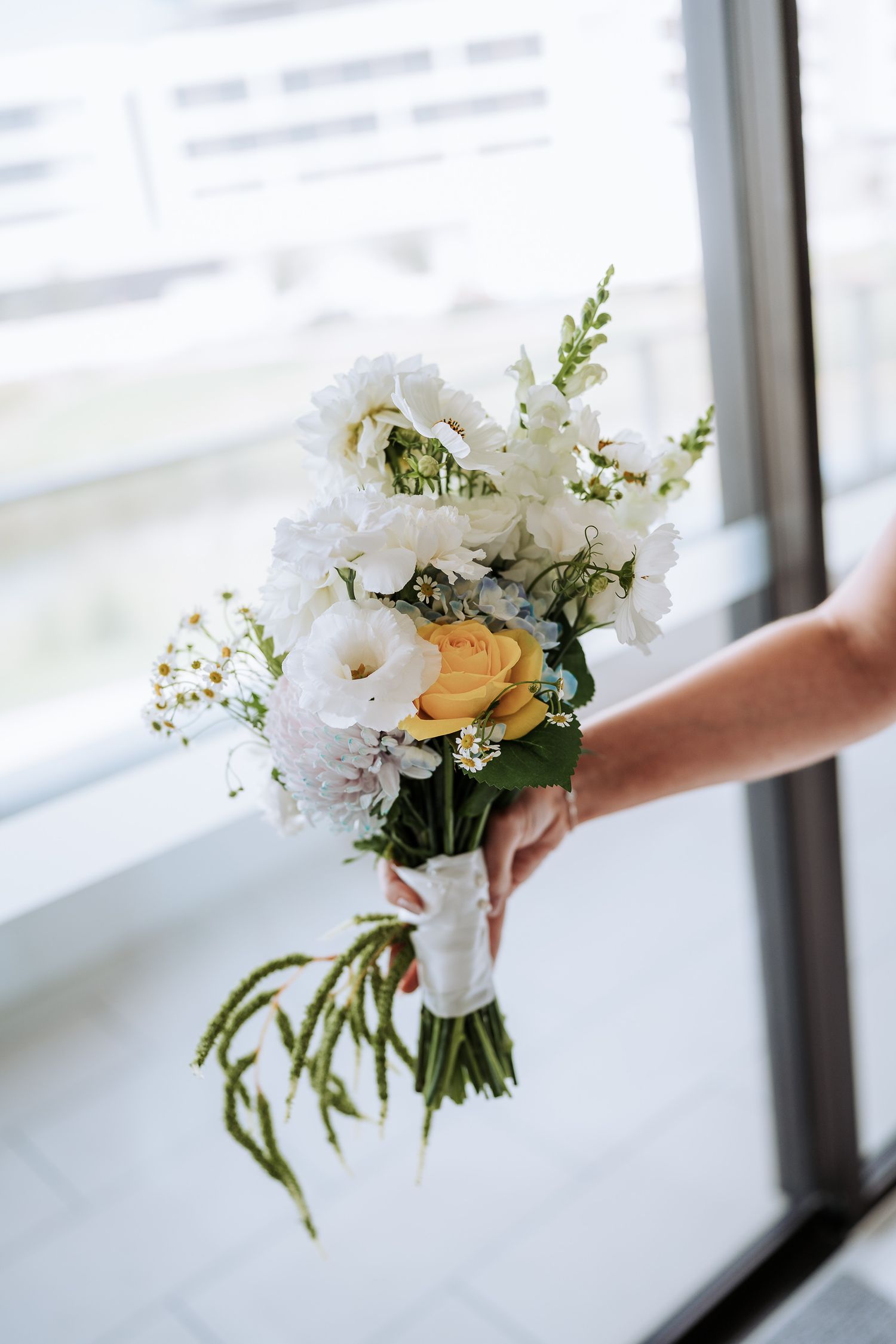A delicate white floral bouquet with greenery is held near a window in natural light, captured in four sequential frames.