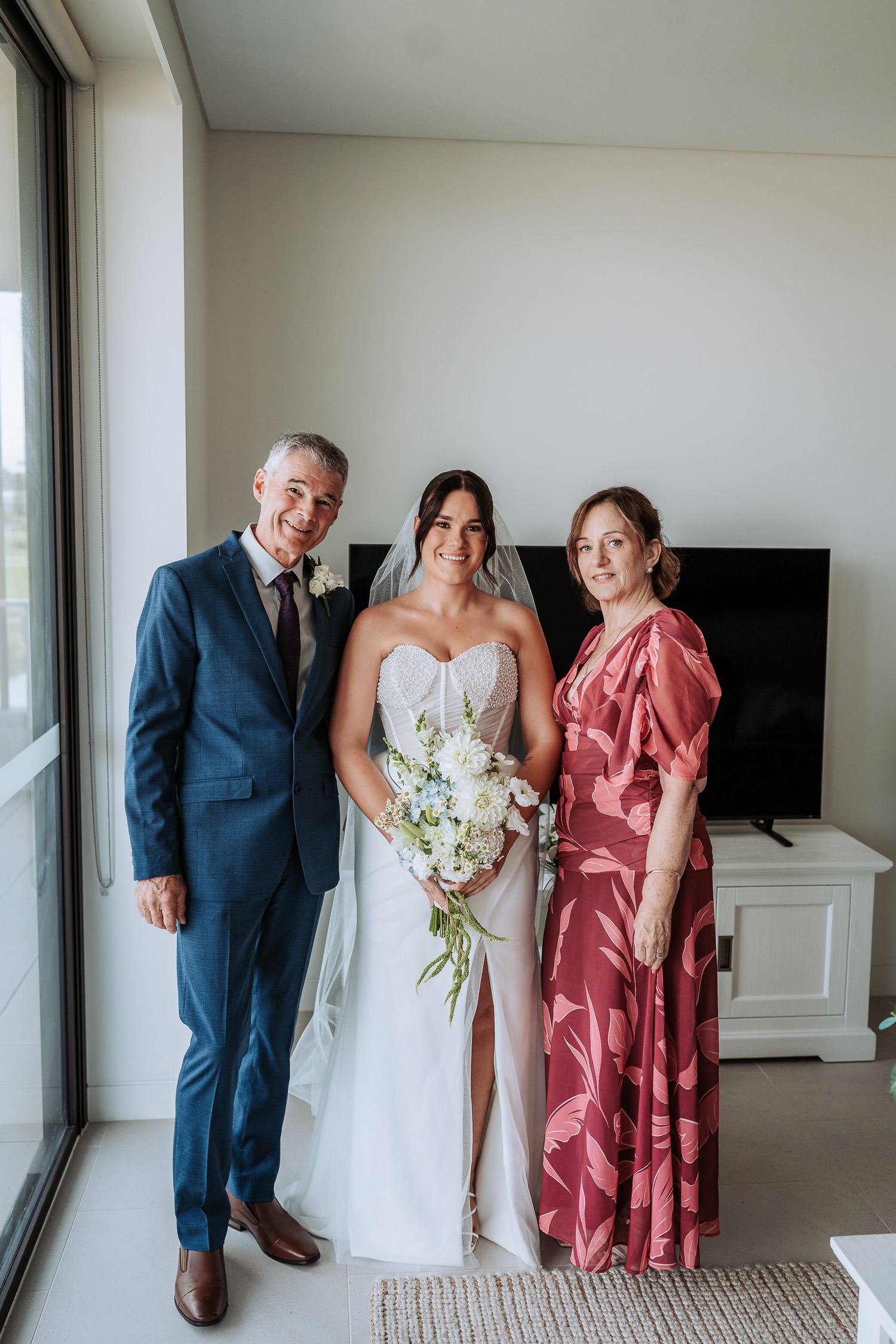 Wedding party poses in a bright indoor space with the bride in white and others in navy and coral attire.