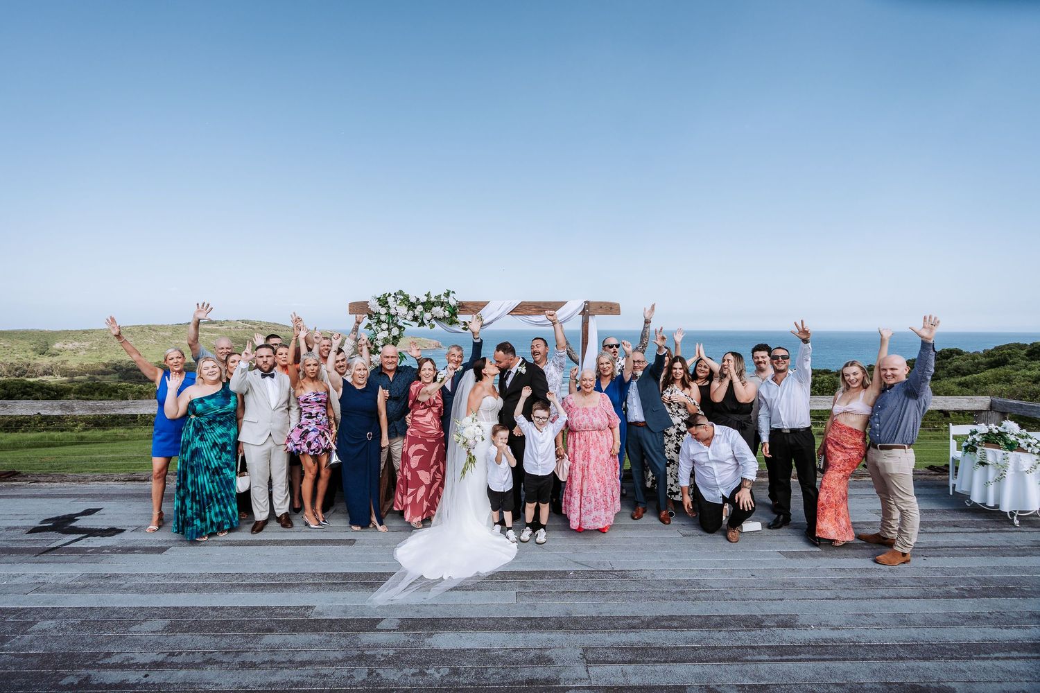 A panoramic series of group photos taken outdoors at a wedding celebration with colorful attire against a scenic backdrop.