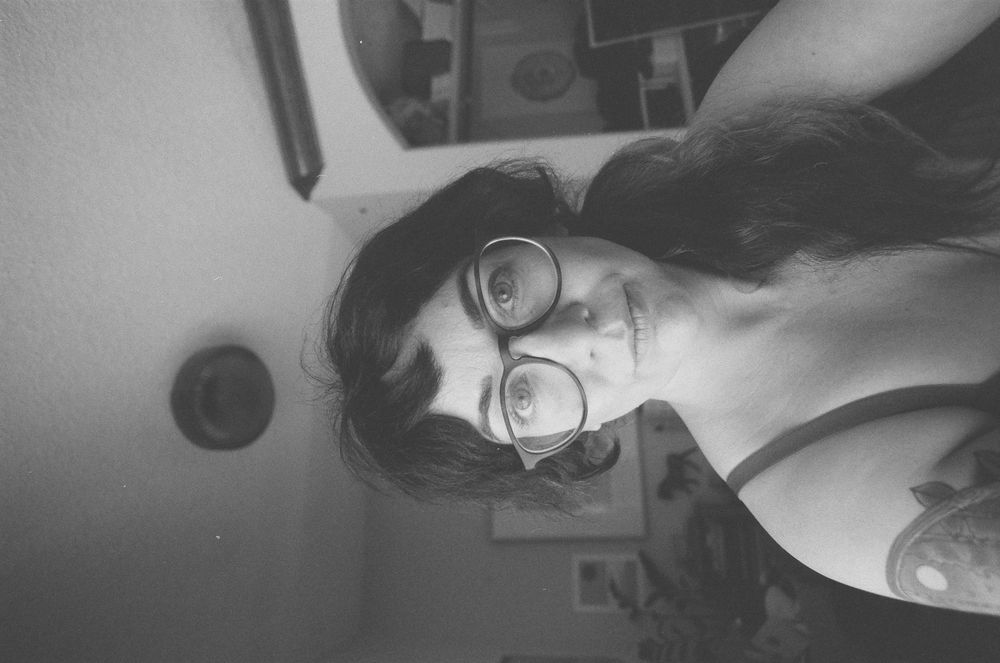 Black and white selfie of a young woman with round glasses and dark hair.