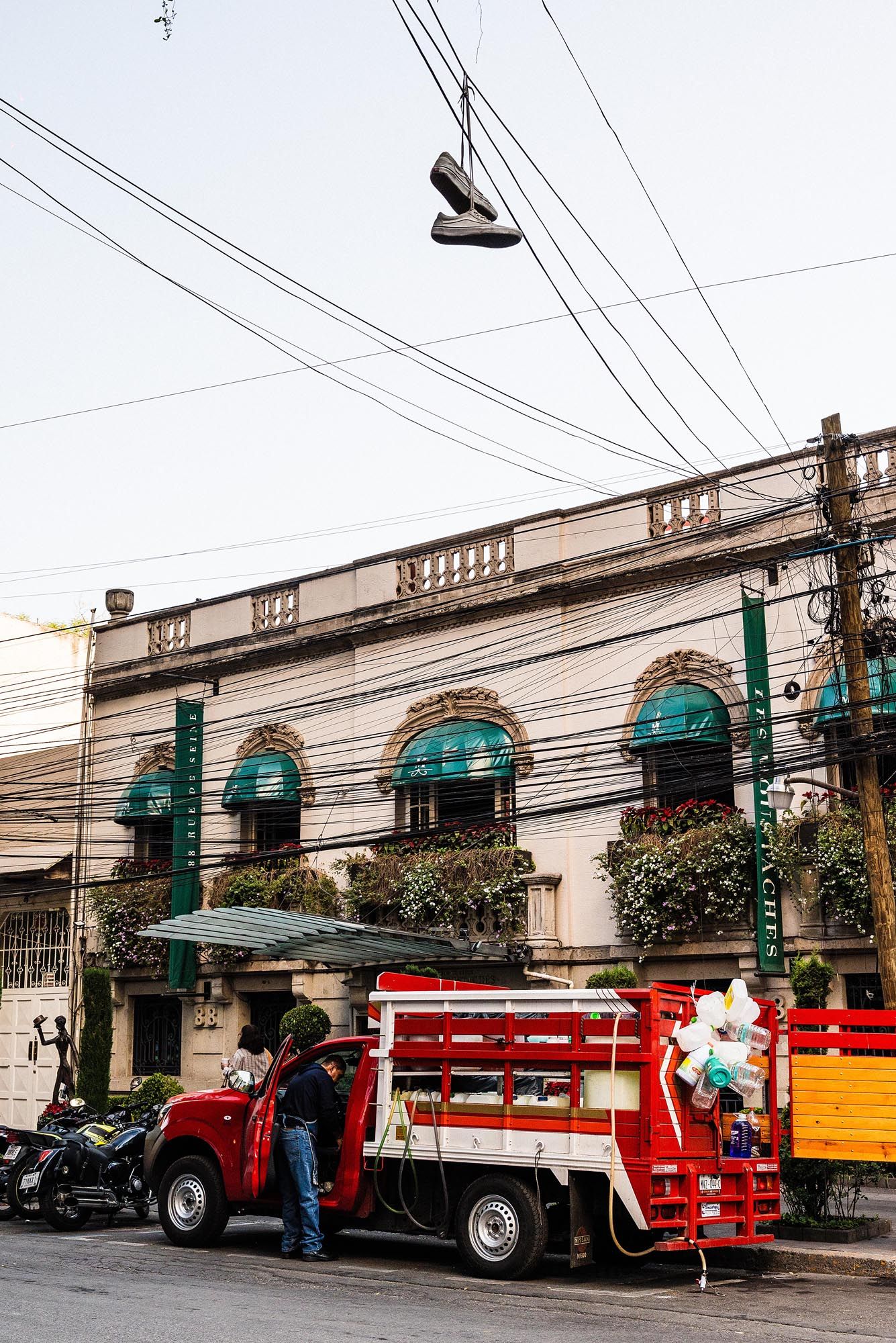 A vintage building with green awnings and a red delivery truck parked outside on an urban street with hanging shoes overhead.