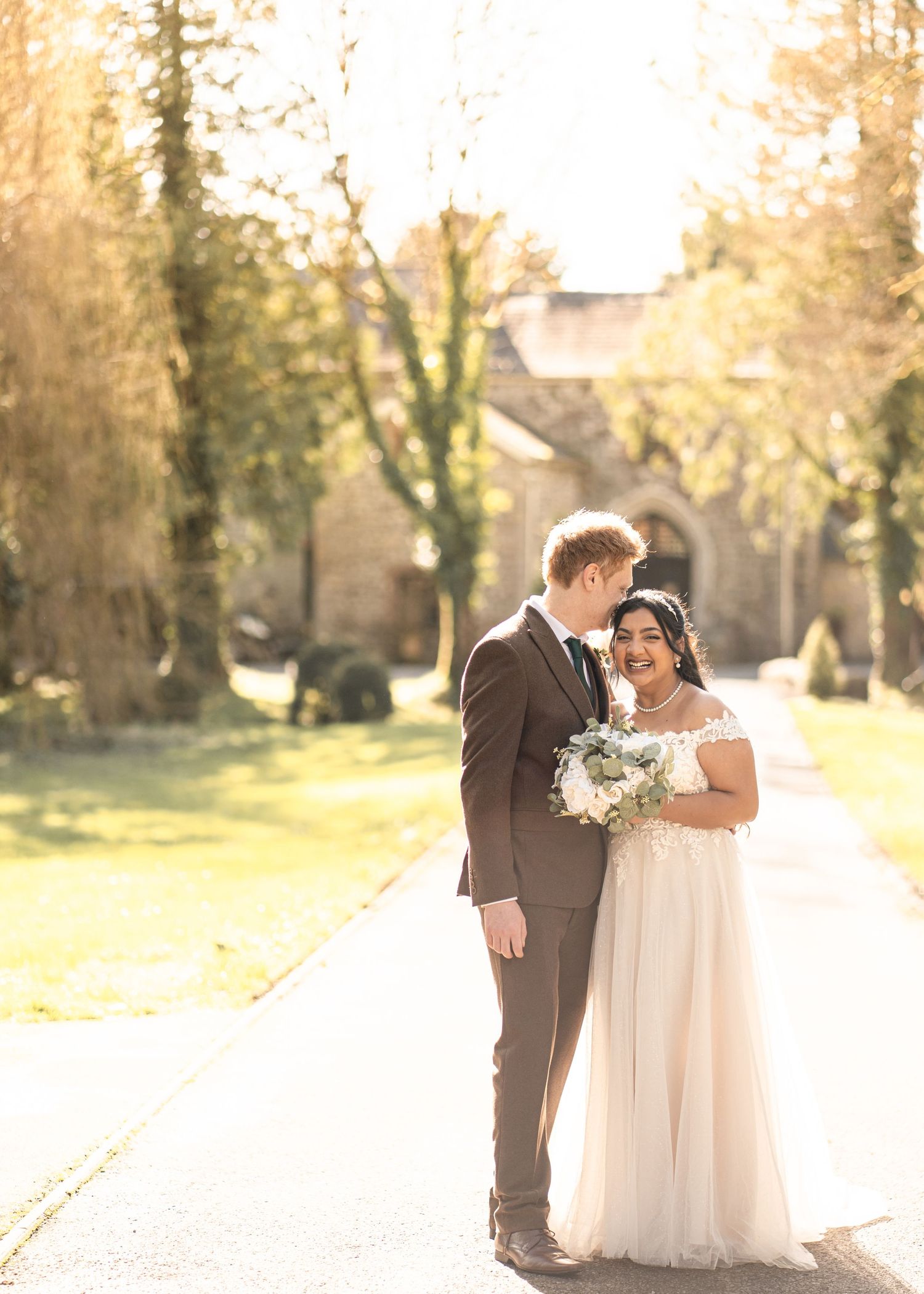 A couple shares a romantic moment in a sun-drenched garden path during their wedding photoshoot.