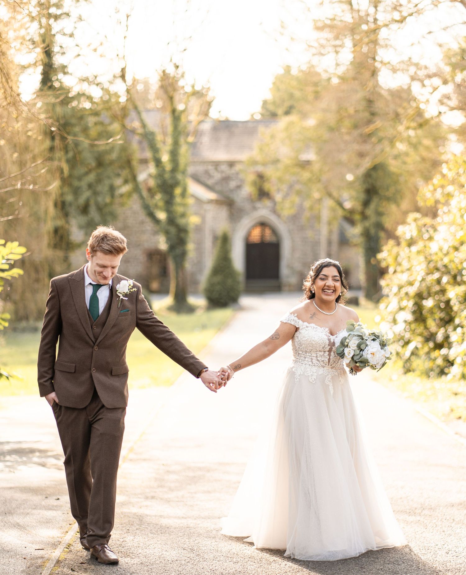 A couple shares a romantic moment walking hand in hand through a sunlit garden path in autumn.