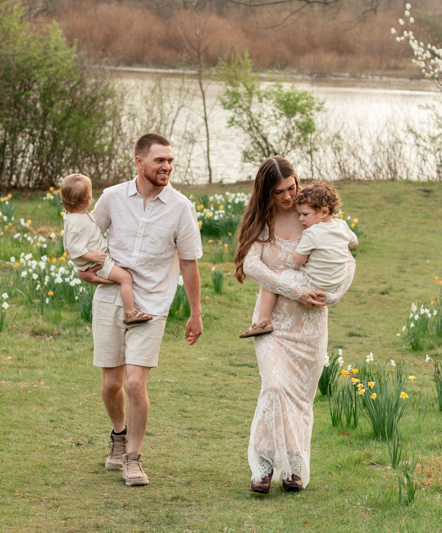 A family in white outfits plays together in a spring garden with blooming daffodils along the water's edge.Family, senior, and wedding photo