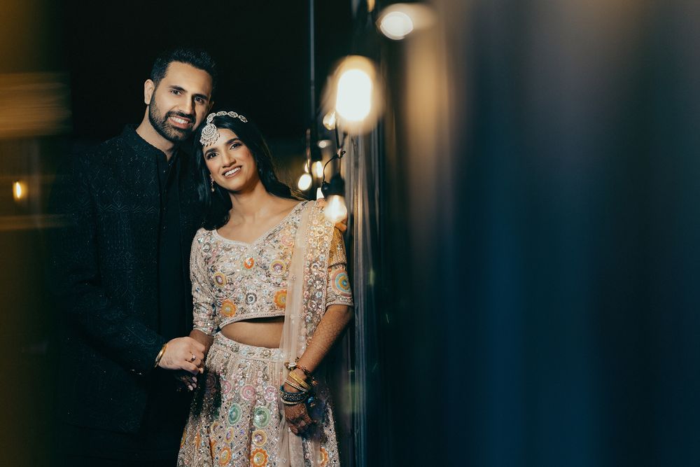 A couple poses together in elegant formal attire at an indoor venue with warm lighting.