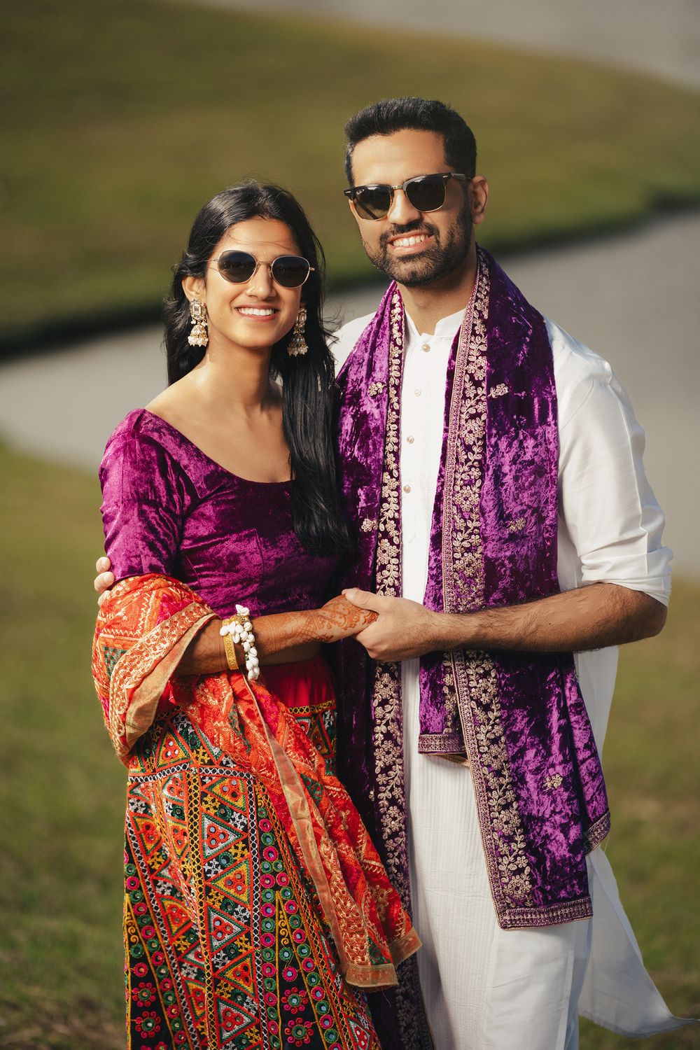 A couple wearing sunglasses and colorful traditional outfits pose together outdoors in a series of romantic photos.