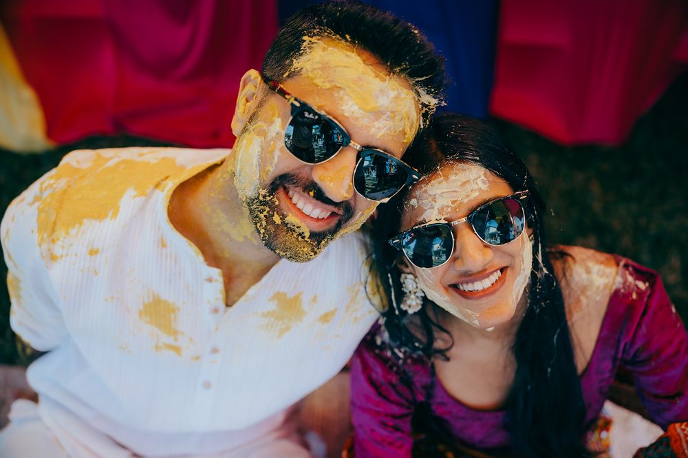 Two people in sunglasses share a joyful moment while wearing white shirts against a dark red background.