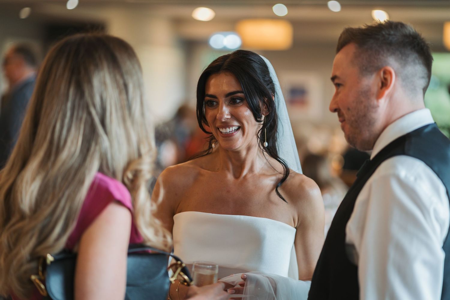 A couple shares a romantic kiss during their wedding reception while guests mingle in the background.
