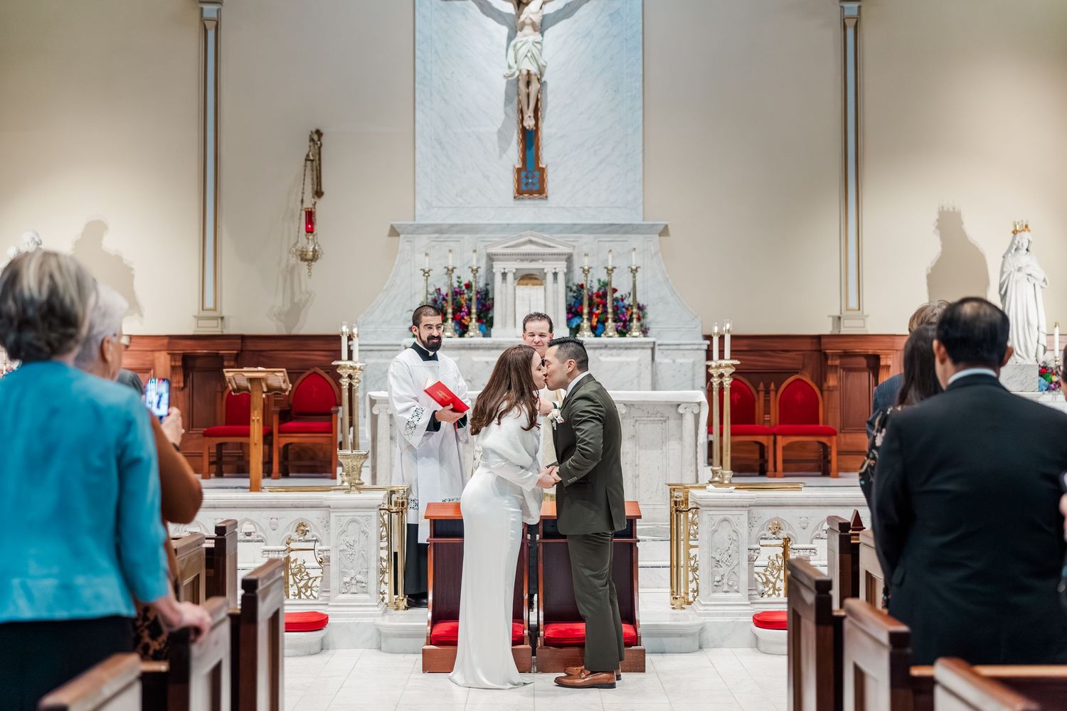 A church wedding ceremony takes place with guests seated in wooden pews as the couple stands at the altar.