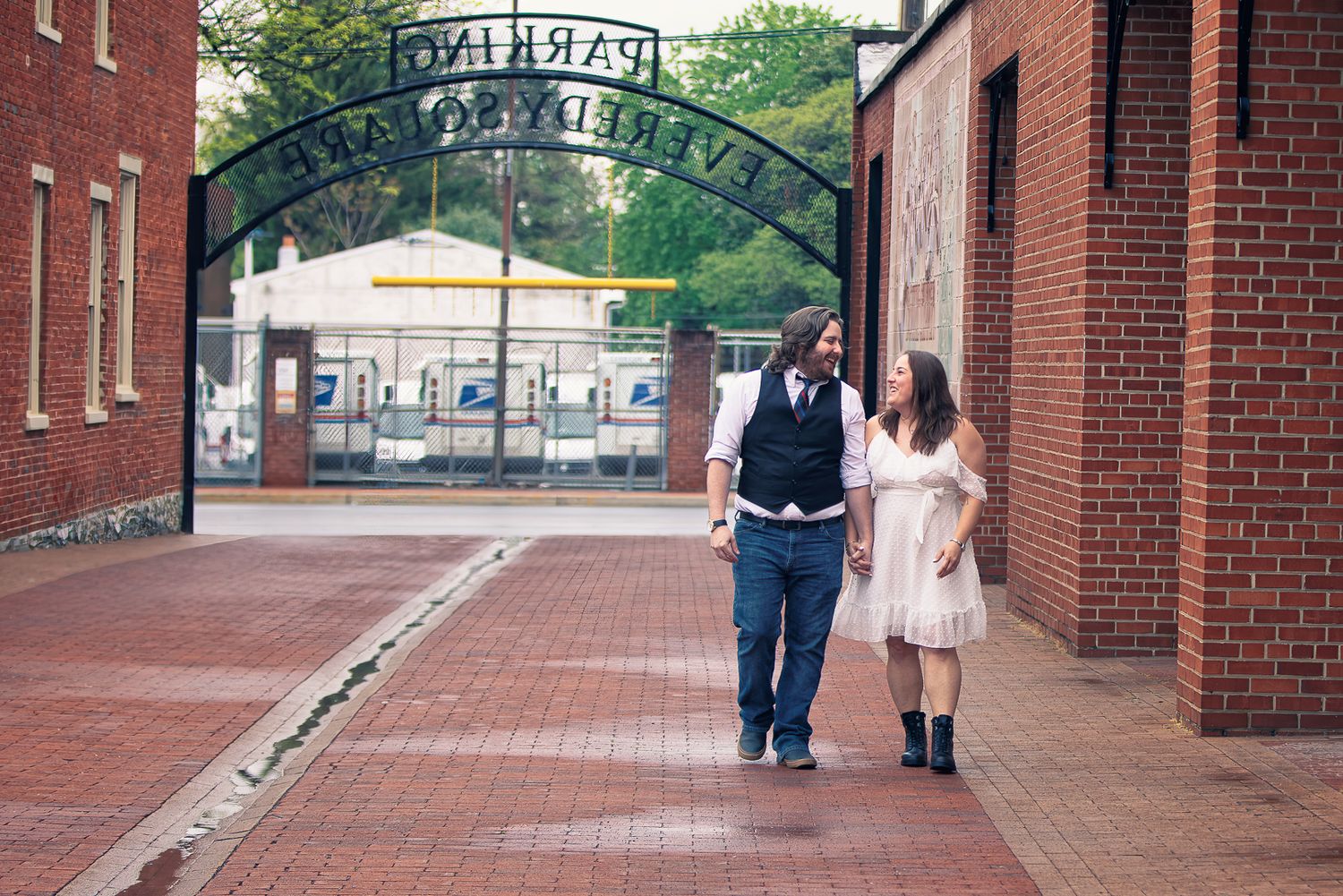 People walk along a brick-paved path under an ornate metal archway entrance at a university campus.