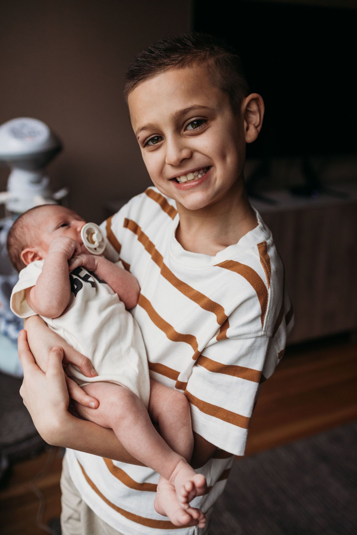 A child in a white and brown striped shirt holds and gazes lovingly at a newborn baby in a series of photos.