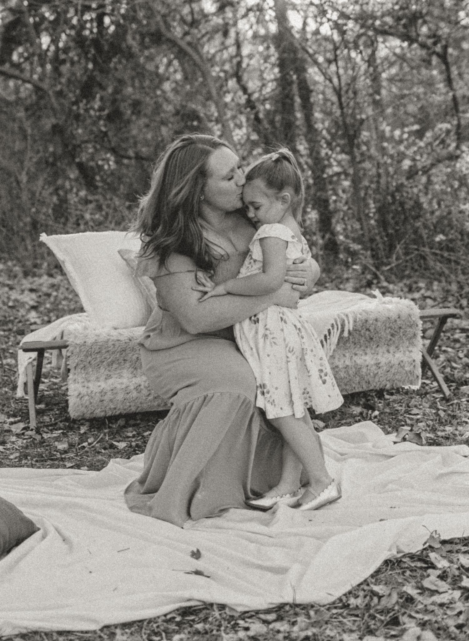A touching black and white portrait of a tender moment between a mother and child sitting on a blanket outdoors.