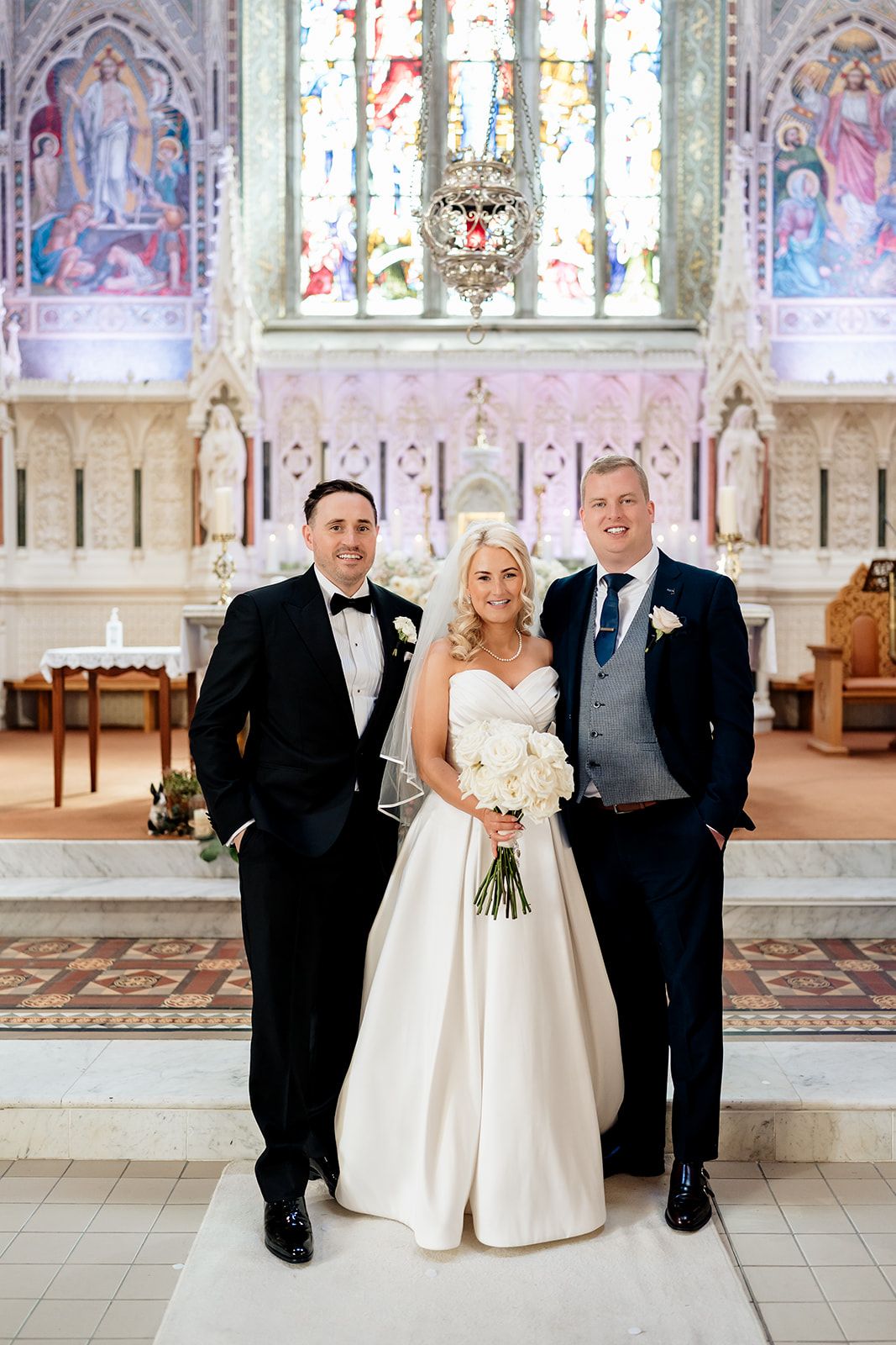 Wedding celebration inside ornate church sanctuary with stained glass windows and decorative altar in background.